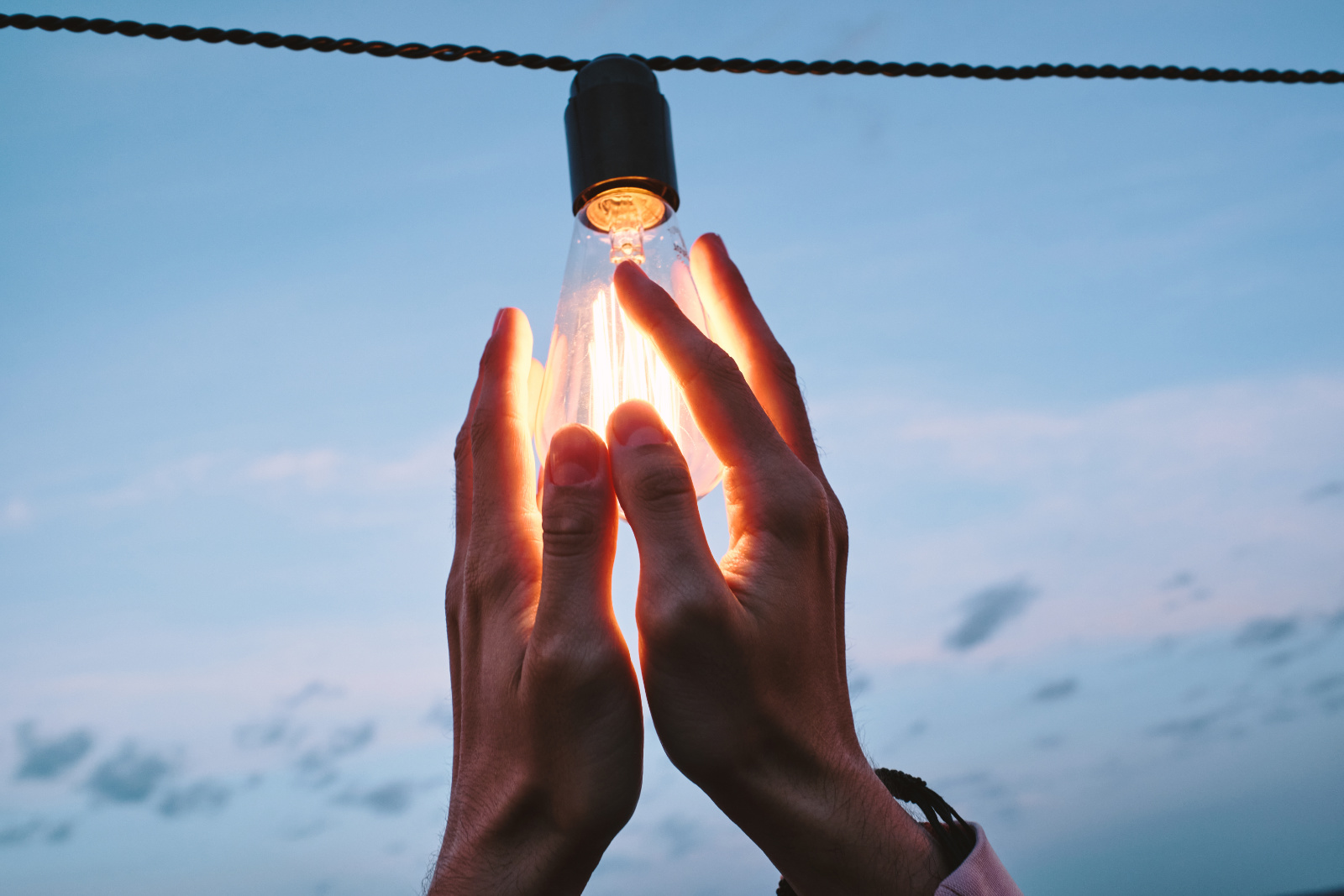 Hands of young man holding electric bulb hanging on wire
