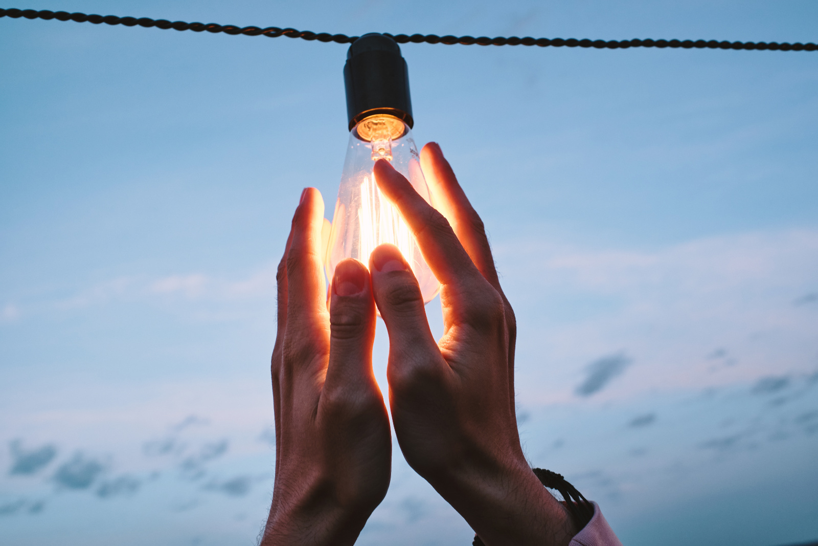 Hands Of Young Man Holding Electric Bulb Hanging On Wire