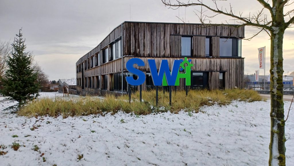 Gebäude mit Holzfassade und Schriftzug SWH im Schneegarten bei bewölktem Himmel